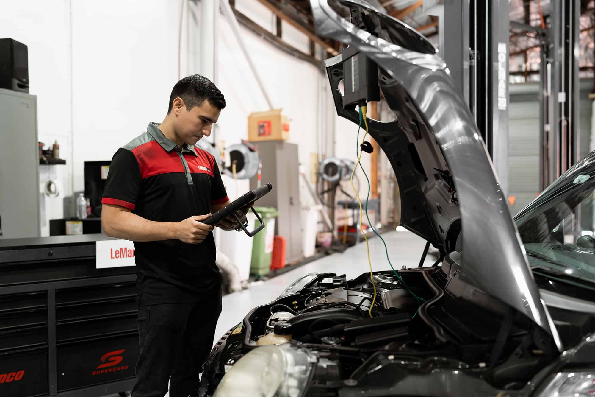 A car mechanic testing the brakes with a tablet device during a logbook servicing.