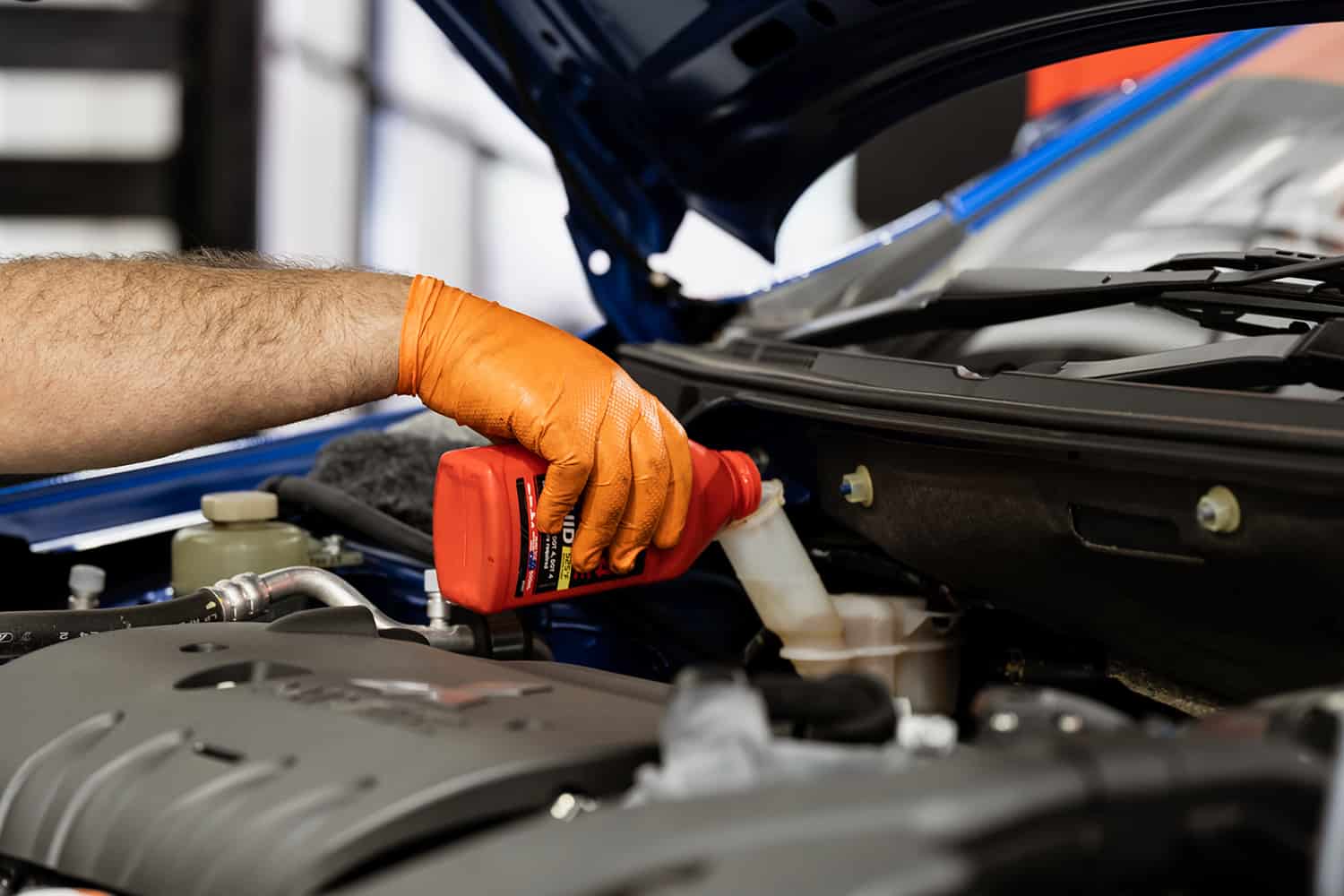 Mechanic wearing orange gloves pouring fluid