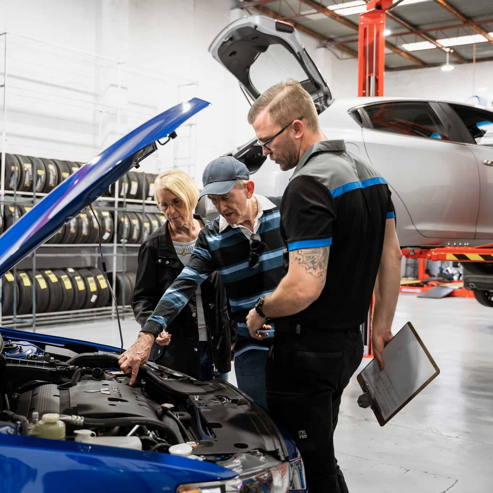 A car mechanic talking to customers about their car, next to an open car bonnet
